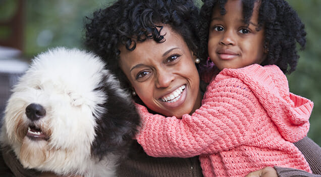 Black mother hugging daughter and dog outdoors