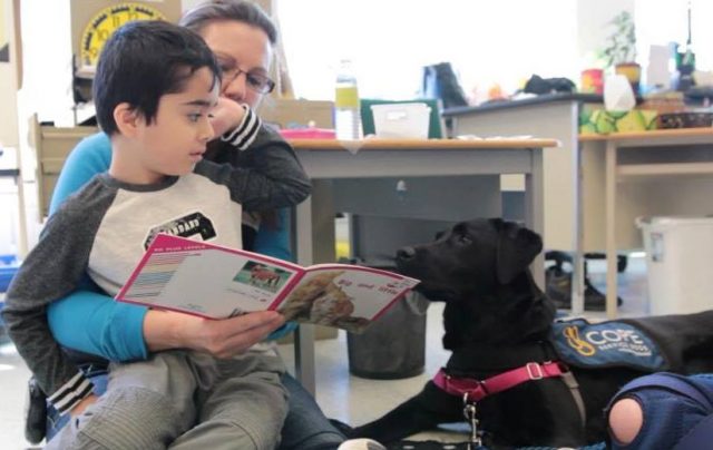 Little boy reading to Black COPE dog